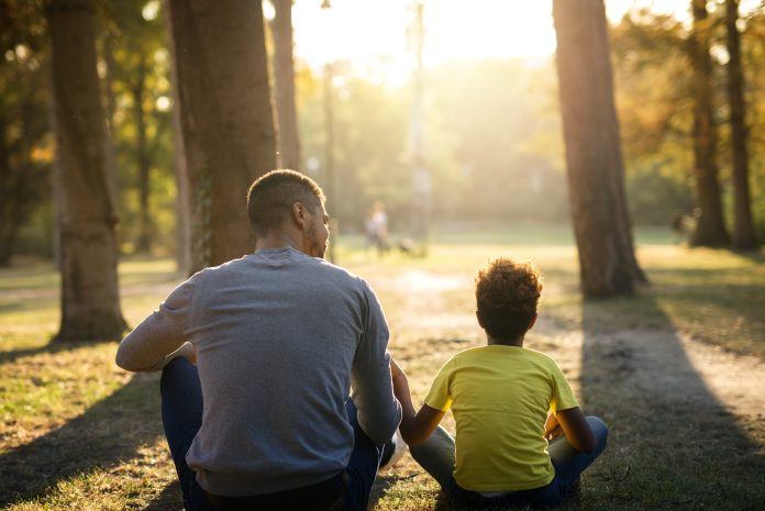 Father and daughter sitting on grass in park enjoying sunset together. bem-estar parental proativo